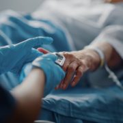 Hospital Ward: Senior Female Resting in a Bed Nurse Has Finger Heart Rate Monitor / Pulse Oximeter showing Pulse. Anonymous Nurse Checks Vitals of Woman Getting well after Surgery. Descubra o que é a Doença Ocupacional e como pode te atingir