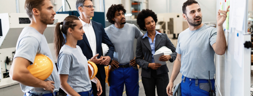 Happy manual worker presenting the results of business development while giving presentation to company leaders and his team in a factory.